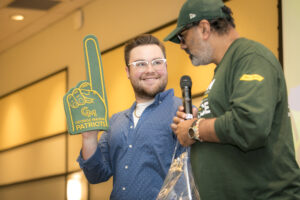 Picture from the raffle, Jordan Emely holding up a George Mason foam finger and looking at Assad Khan holding a mic. John Boal Photography