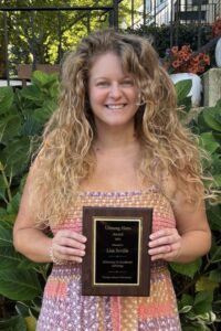 Lisa Sevilla holding the plaque for the Unsung Hero Award for 2025